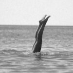 Responsible Diving - Black and White Photo of Legs of a Diving Person Sticking Out of the Water