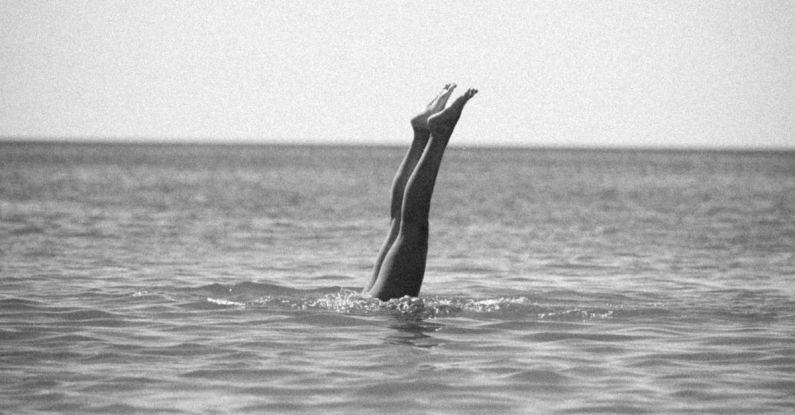 Responsible Diving - Black and White Photo of Legs of a Diving Person Sticking Out of the Water