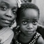 Local Communities - Black and white glad children in casual clothes standing on authentic town street and looking at camera with curiosity