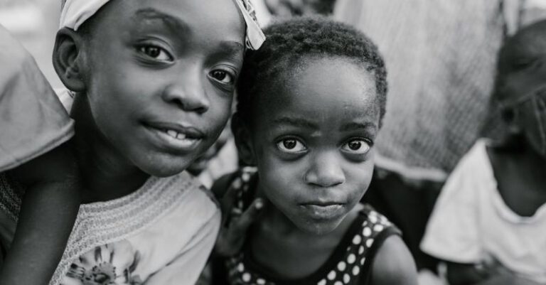 Local Communities - Black and white glad children in casual clothes standing on authentic town street and looking at camera with curiosity