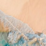 Shorelines - Drone view of anonymous person walking along sandy beach of turquoise sea in sunny day