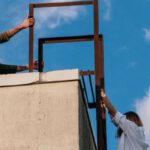 Explorers - Man in Brown Jacket and Blue Denim Jeans Climbing on Brown Concrete Wall