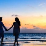 Atolls - Man and Woman Holding Hands Walking on Seashore during Sunrise