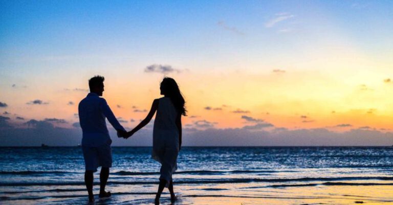 Atolls - Man and Woman Holding Hands Walking on Seashore during Sunrise