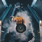 Photography - Man Holding Camera While Squating With Smoke on Face Inside Building