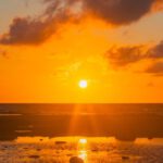 Sharks And Rays - The sun sets over the ocean with clouds in the sky